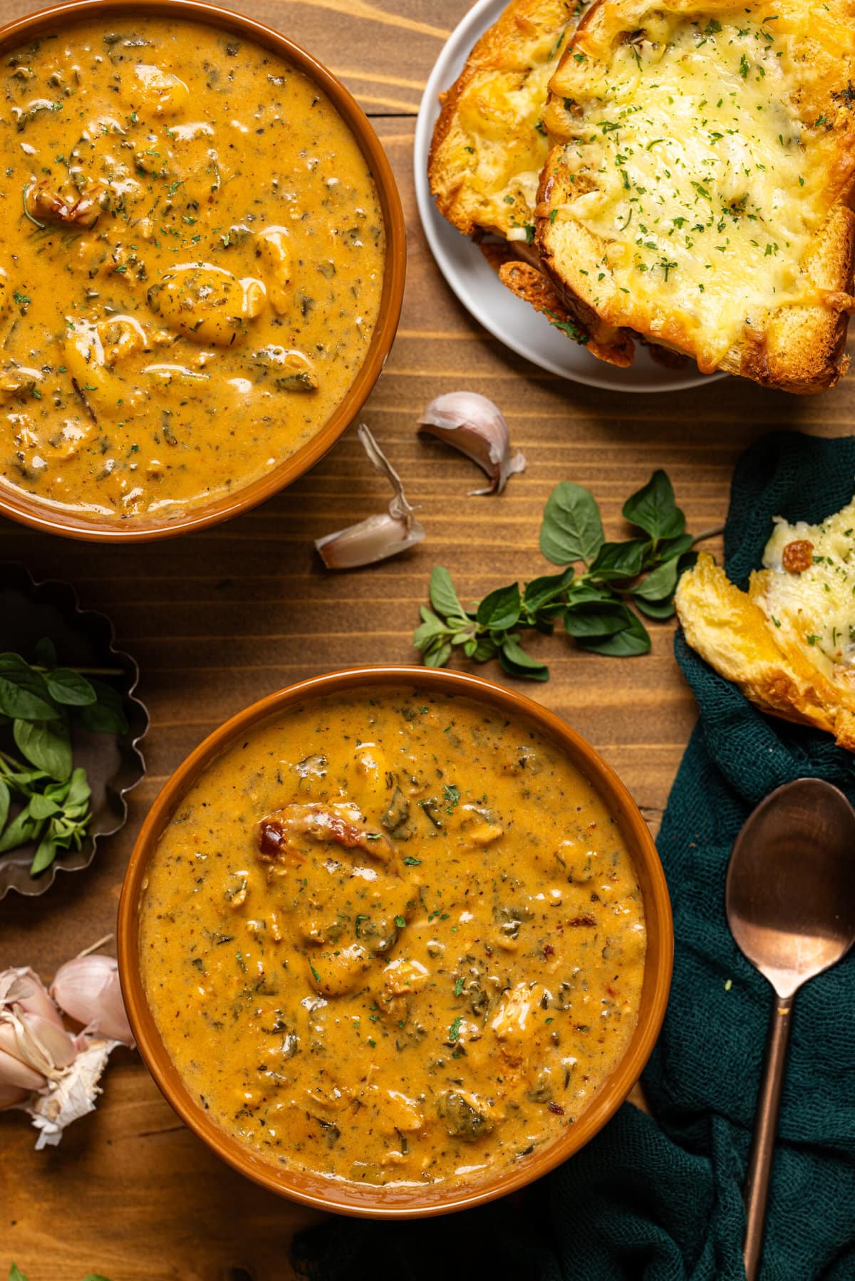 Soup in two bronze bowls with a side of garlic bread, spoon, and garnish. 