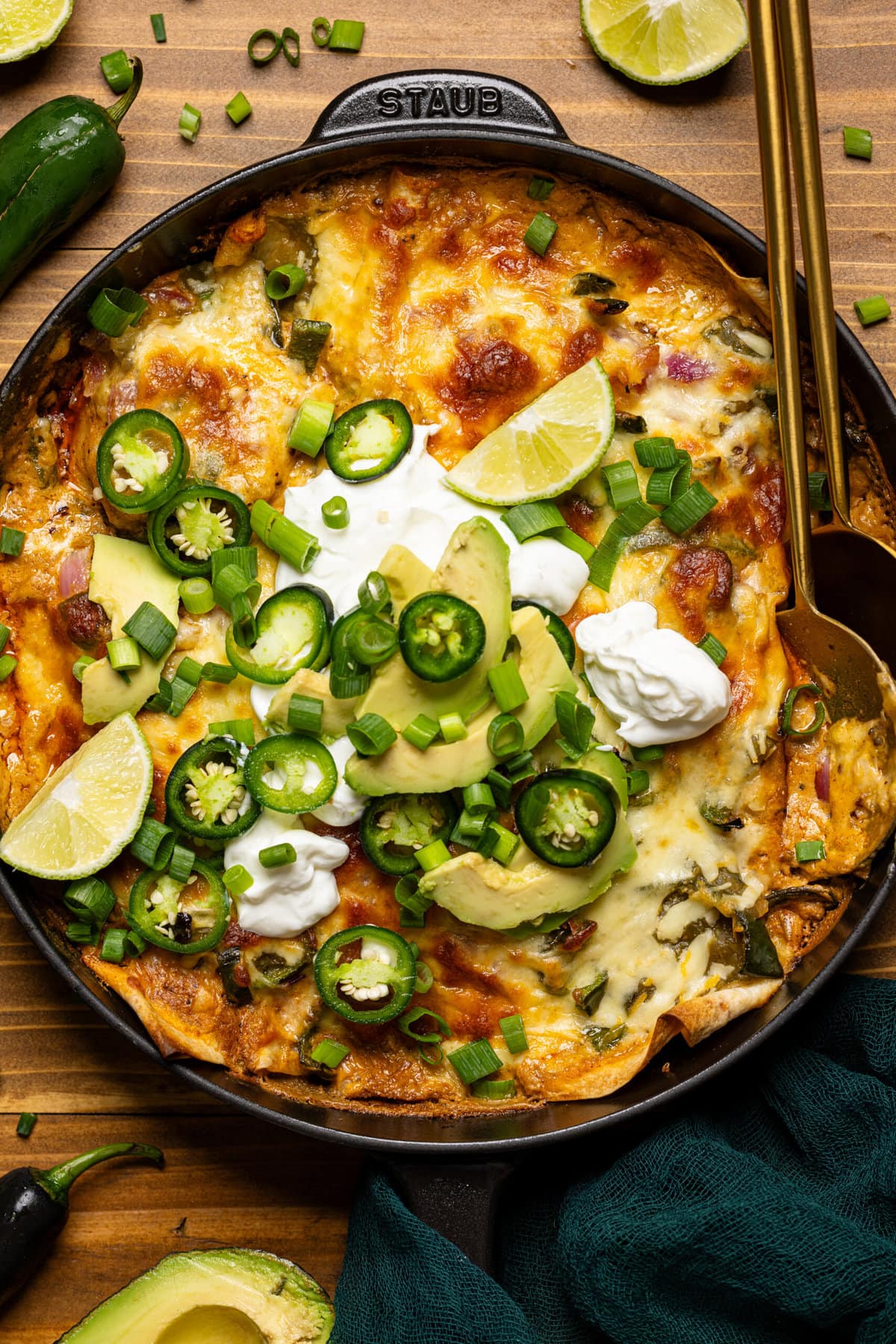 Enchilada in a black skillet with two serving spoons and toppings. 
