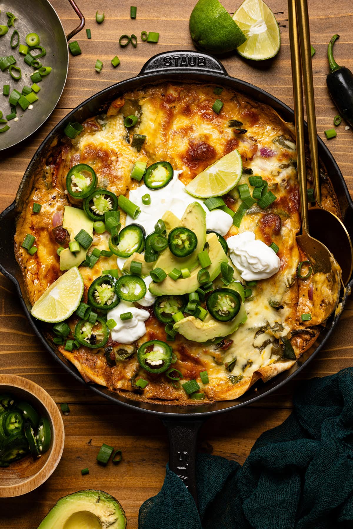 Enchiladas in a skillet with two spoons and garnish. 