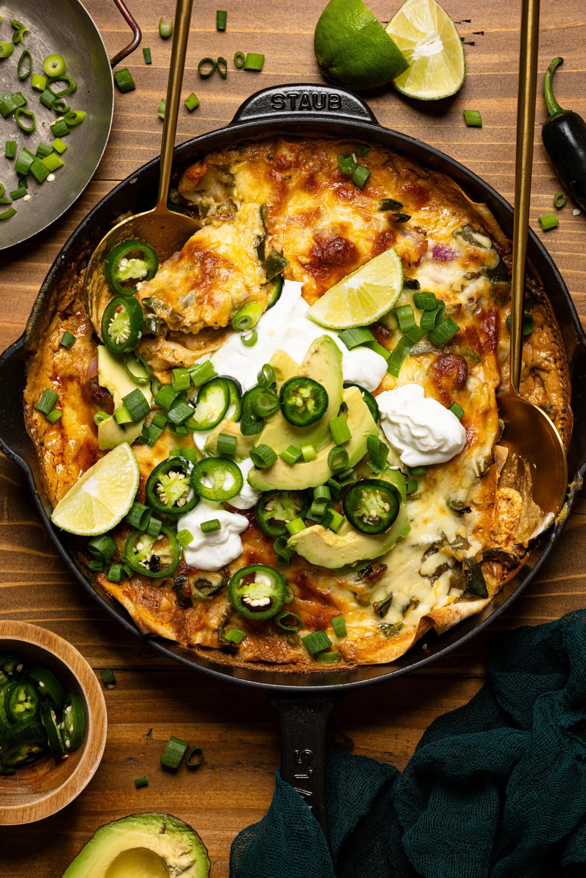 Skillet enchilada with two spoons, lime wedges, and toppings.