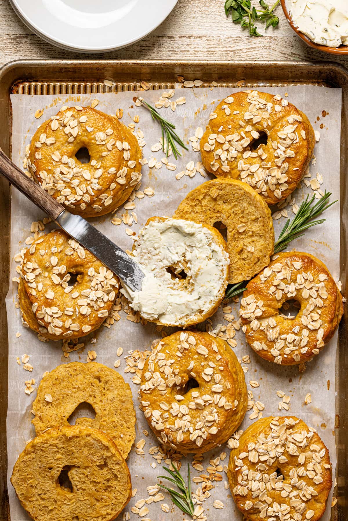 Bagels on a baking sheet with half a bagel with a knife and cream cheese.