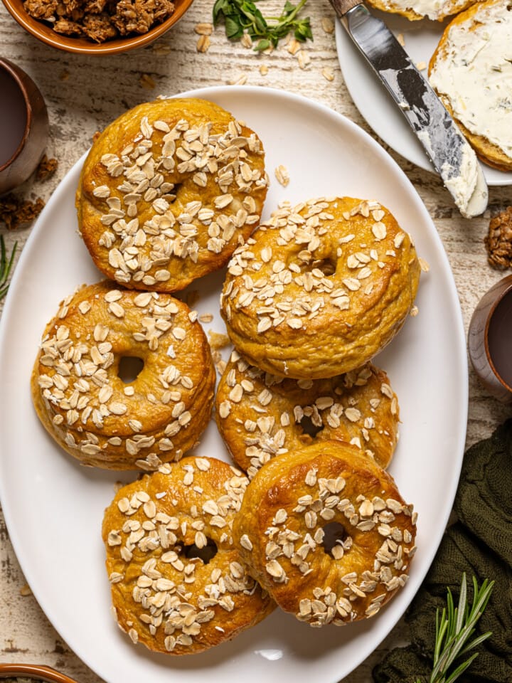 Bagels on a white serving dish with a plater with knife and sliced bagels.