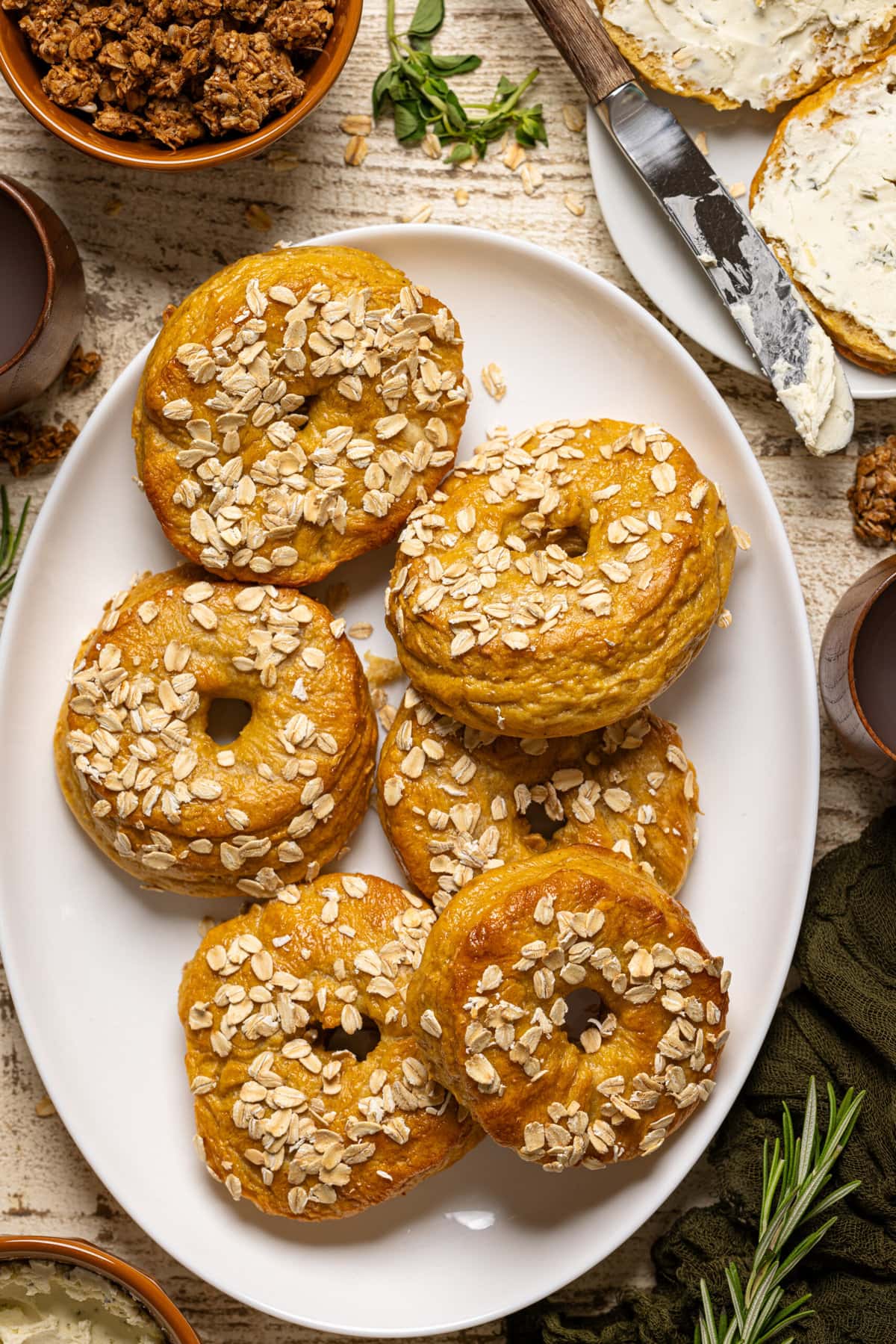 Bagels on a white serving dish with a plater with knife and sliced bagels.