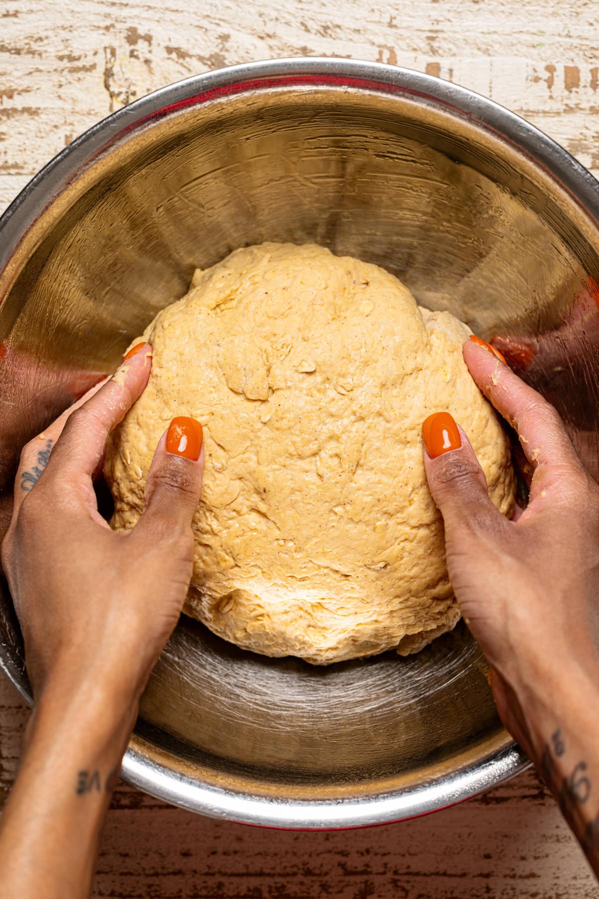 Dough being held with hands in a silver bowl.