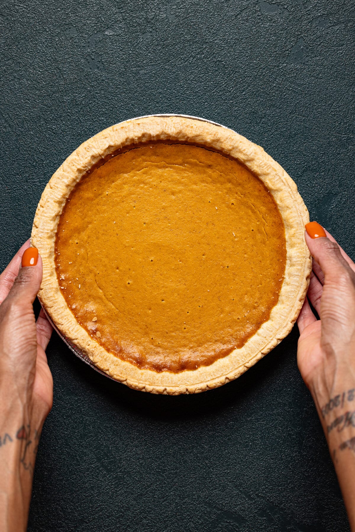 Pumpkin pie being held on a dark green table.