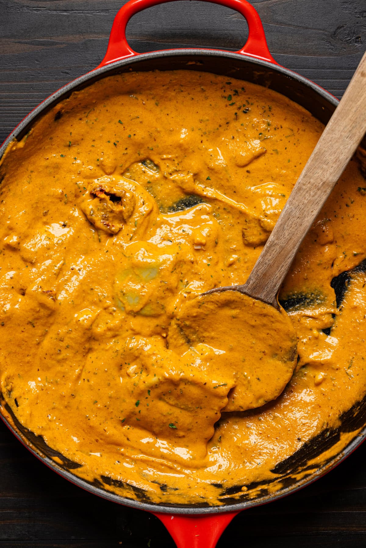 Creamy ravioli in a red skillet with a wooden spoon.