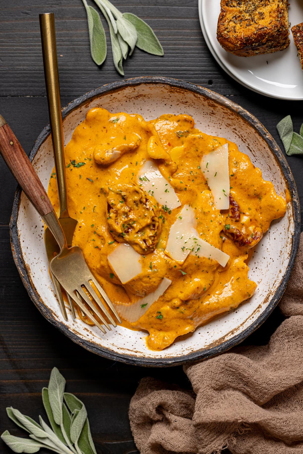 Cozy Sun-dried Tomato Pumpkin Ravioli in a low bowl with two forks, parmesan shavings, and a side of croutons. 