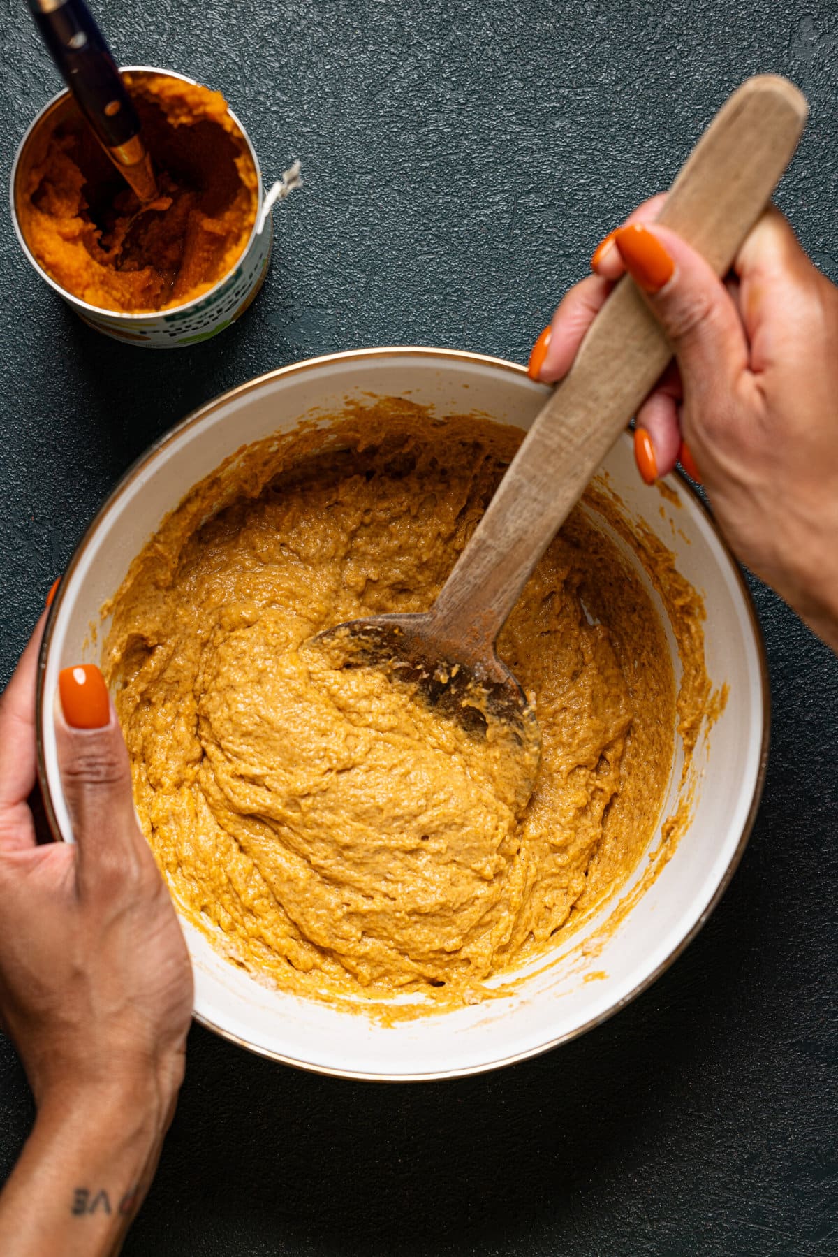 Batter in a white bowl being stirred with a wooden spoon.