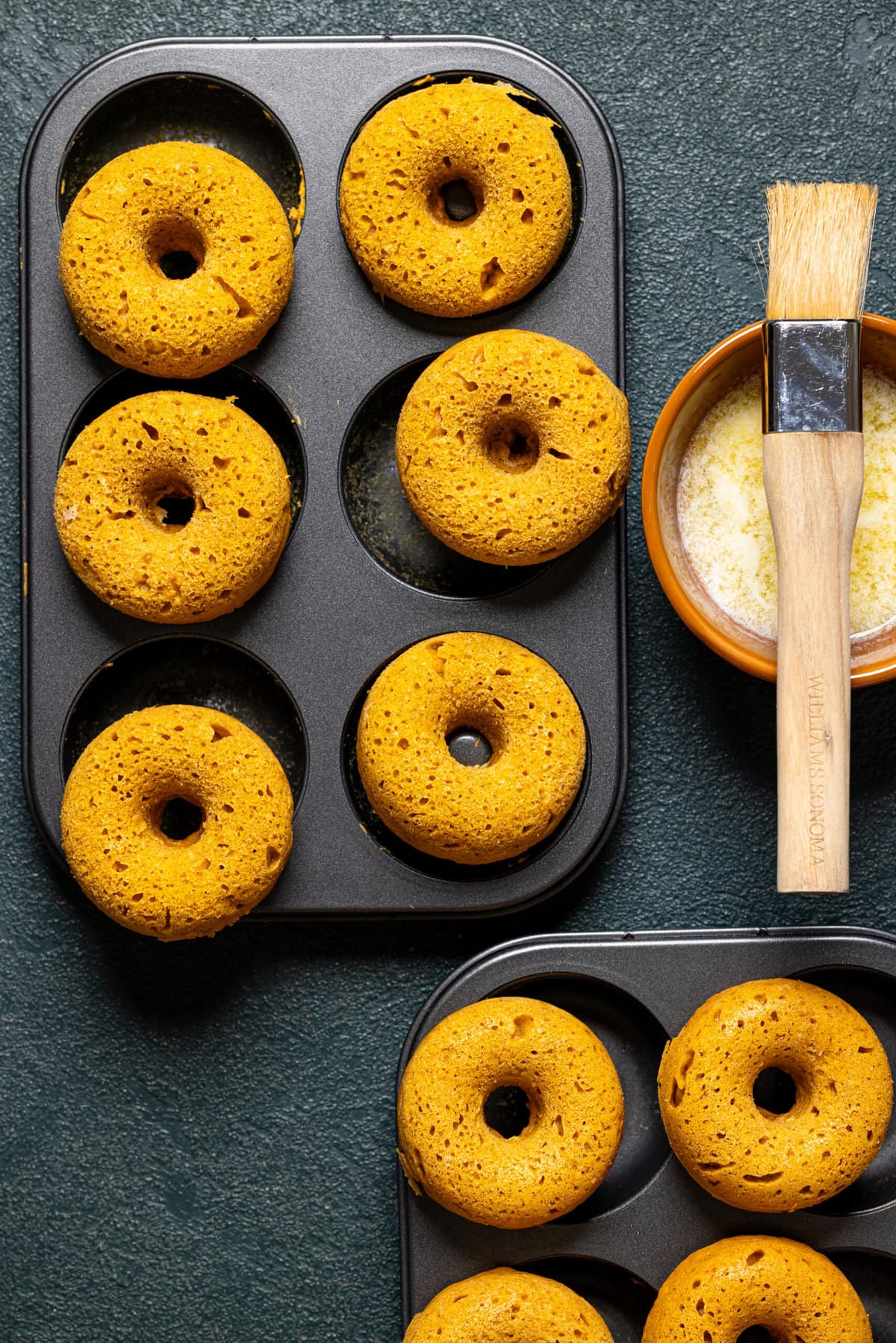 Baked donuts with bowl of butter and brush. 