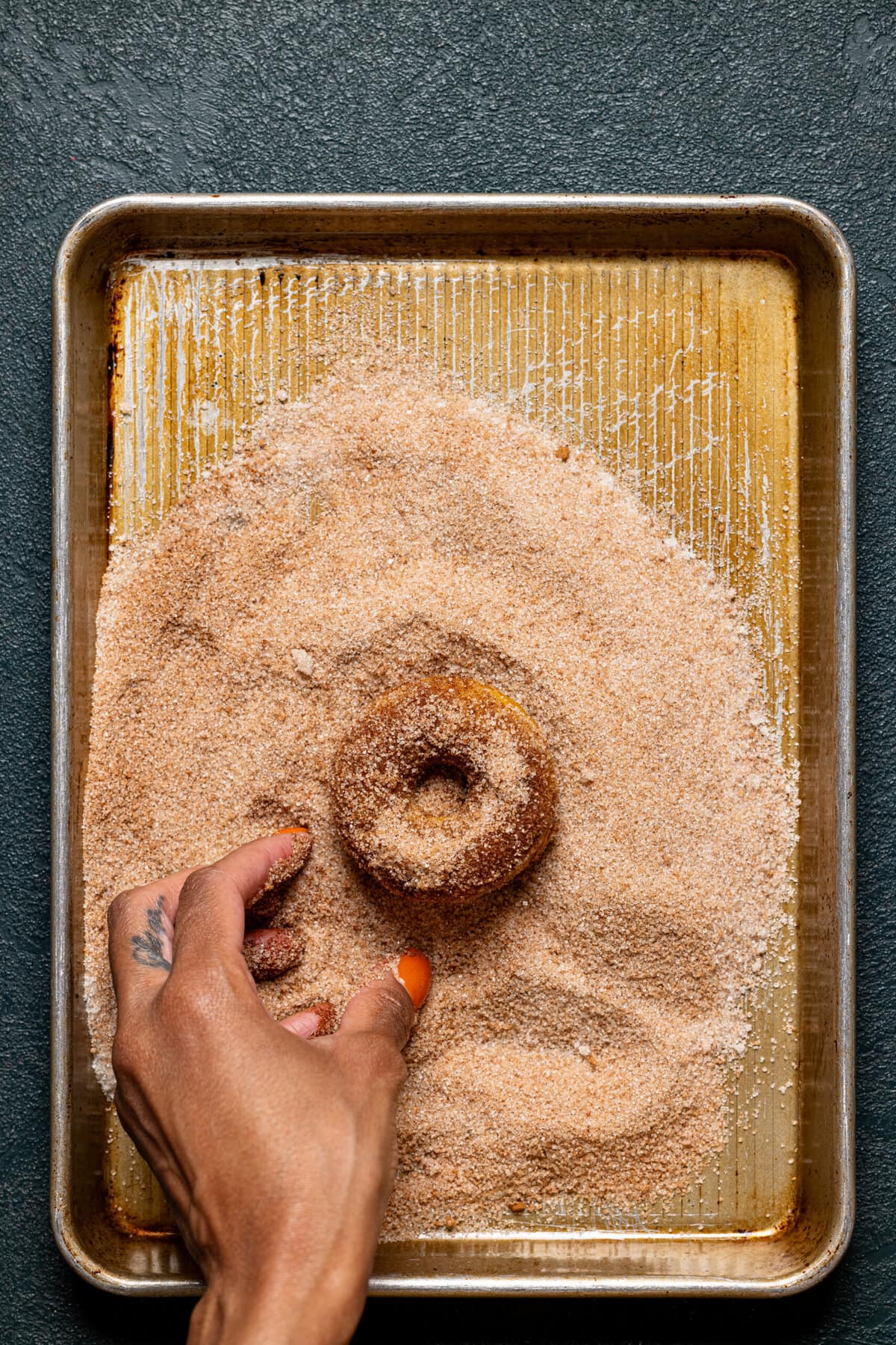 Donut being dusted with sugar on a baking sheet.