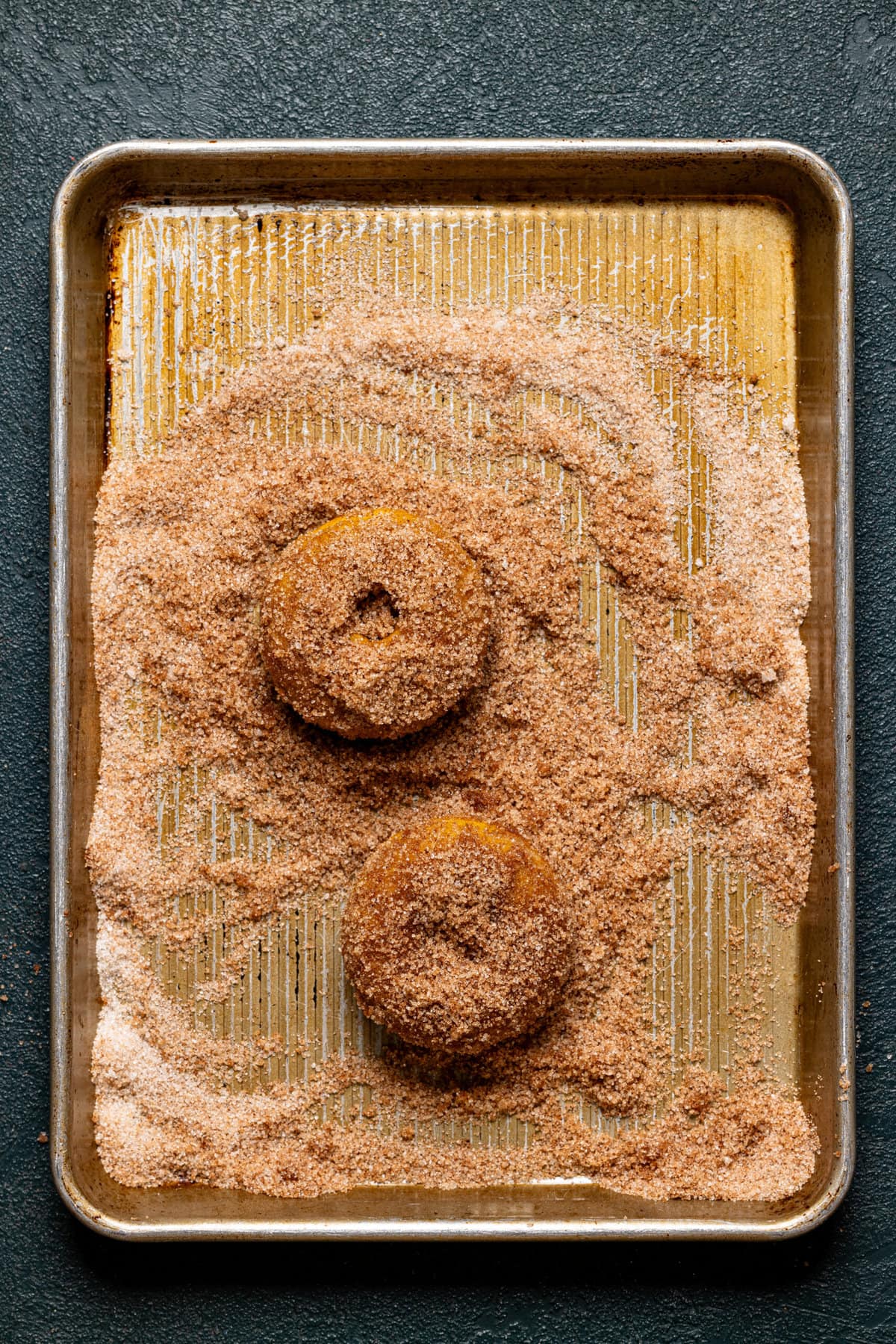 Two donuts covered in sugar on a baking sheet. 