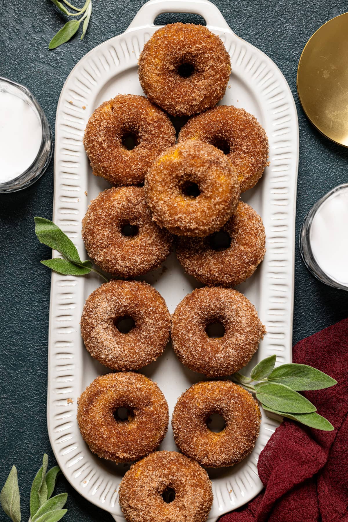 Pumpkin spice donuts on a serving dish with cups of milk on the side.