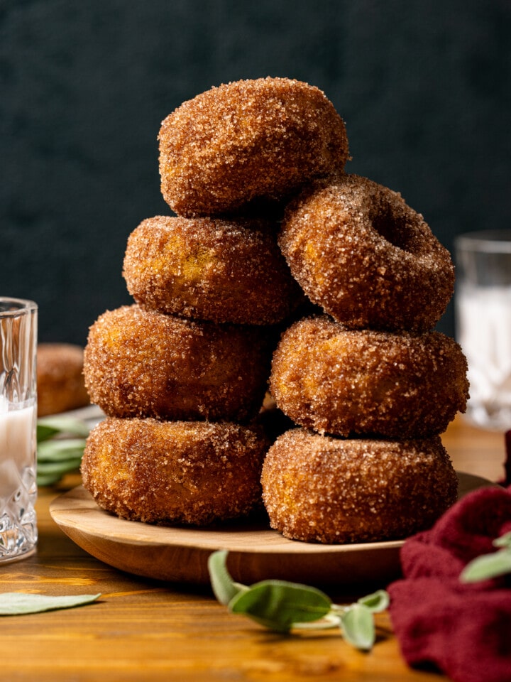 Stacked donuts on a brown plate with glasses of milk.