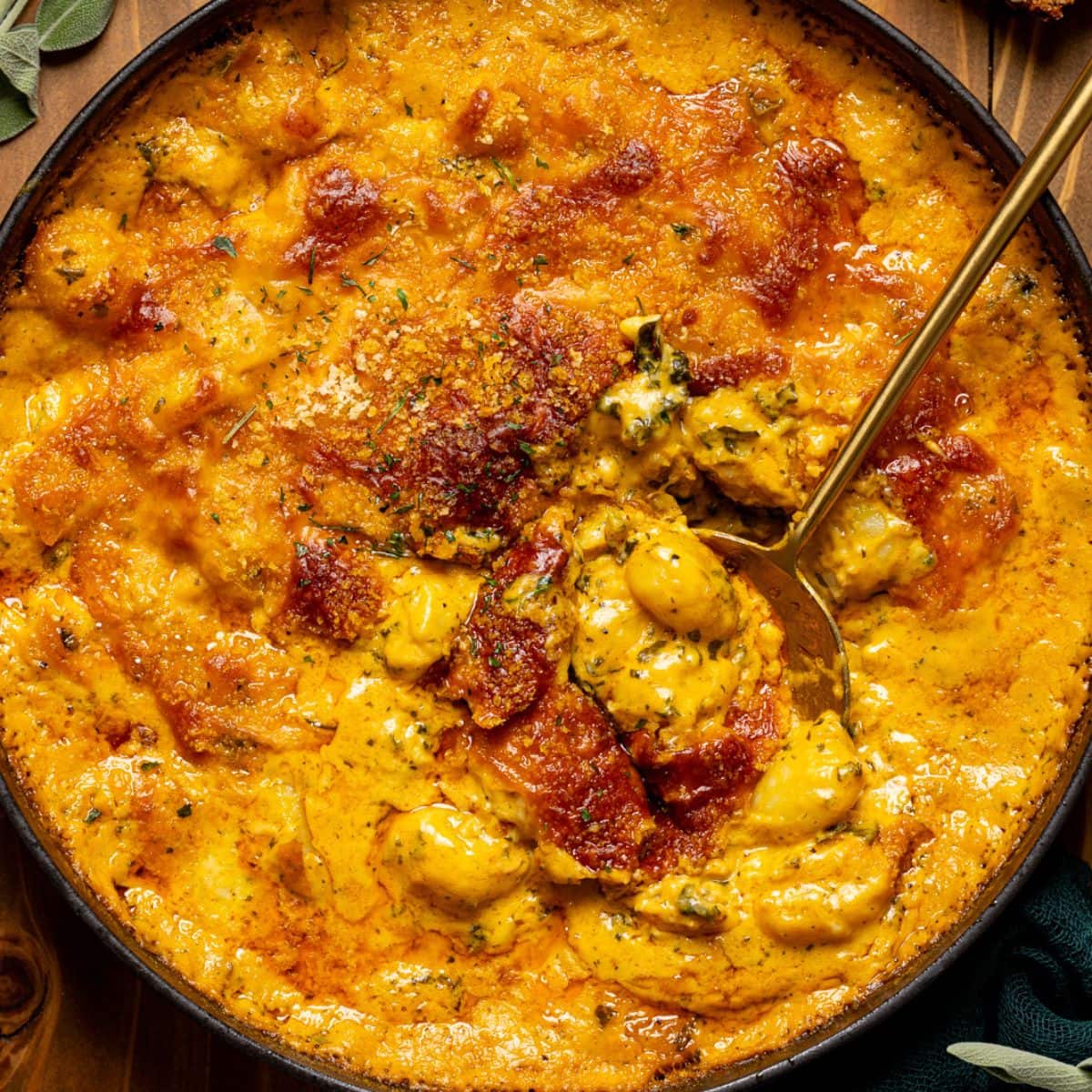 Baked gnocchi in a black skillet with a gold spoon, herbs, and pieces of bread.