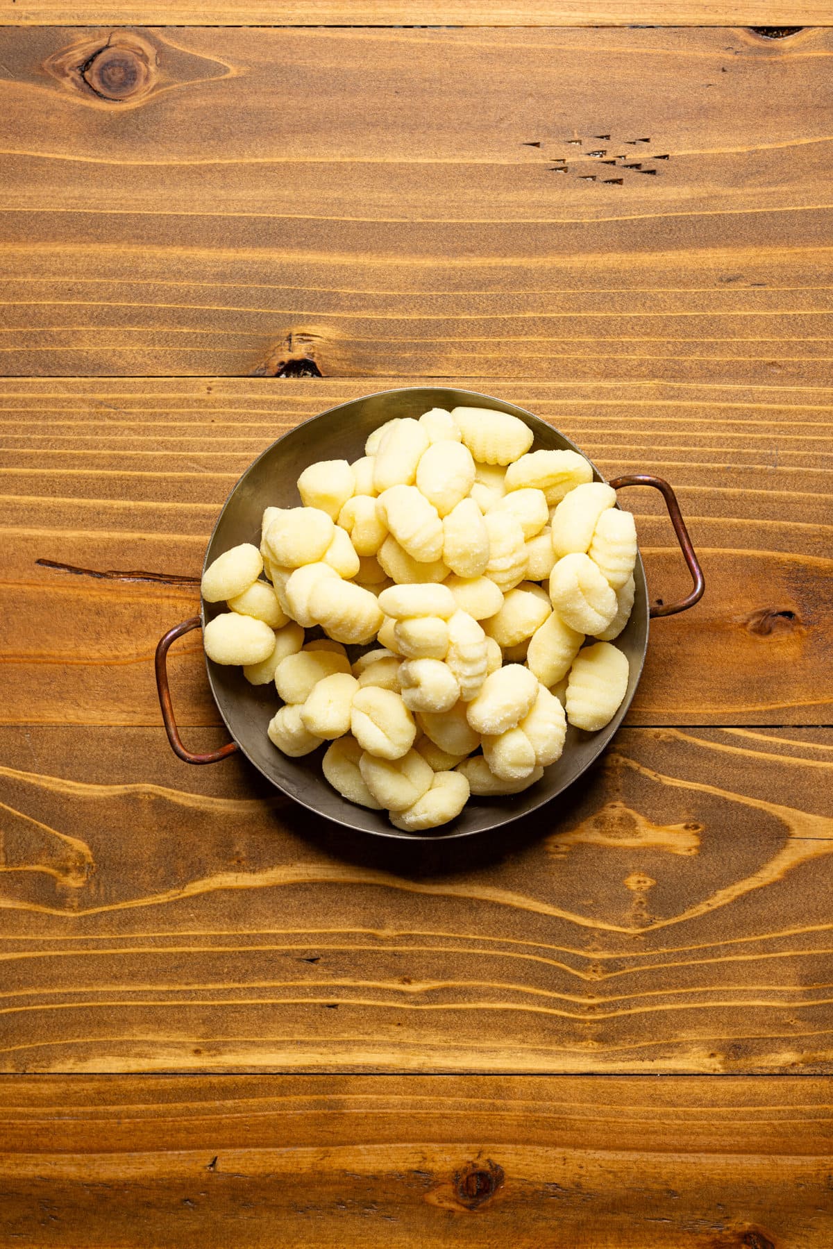 Gnocchi in a bowl on a brown wood table.