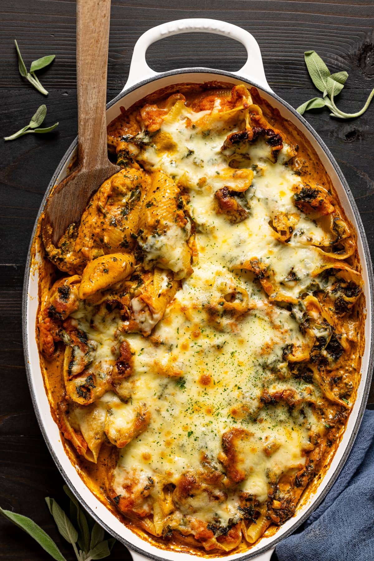 Stuffed baked shells in a baking dish with wooden spoon.