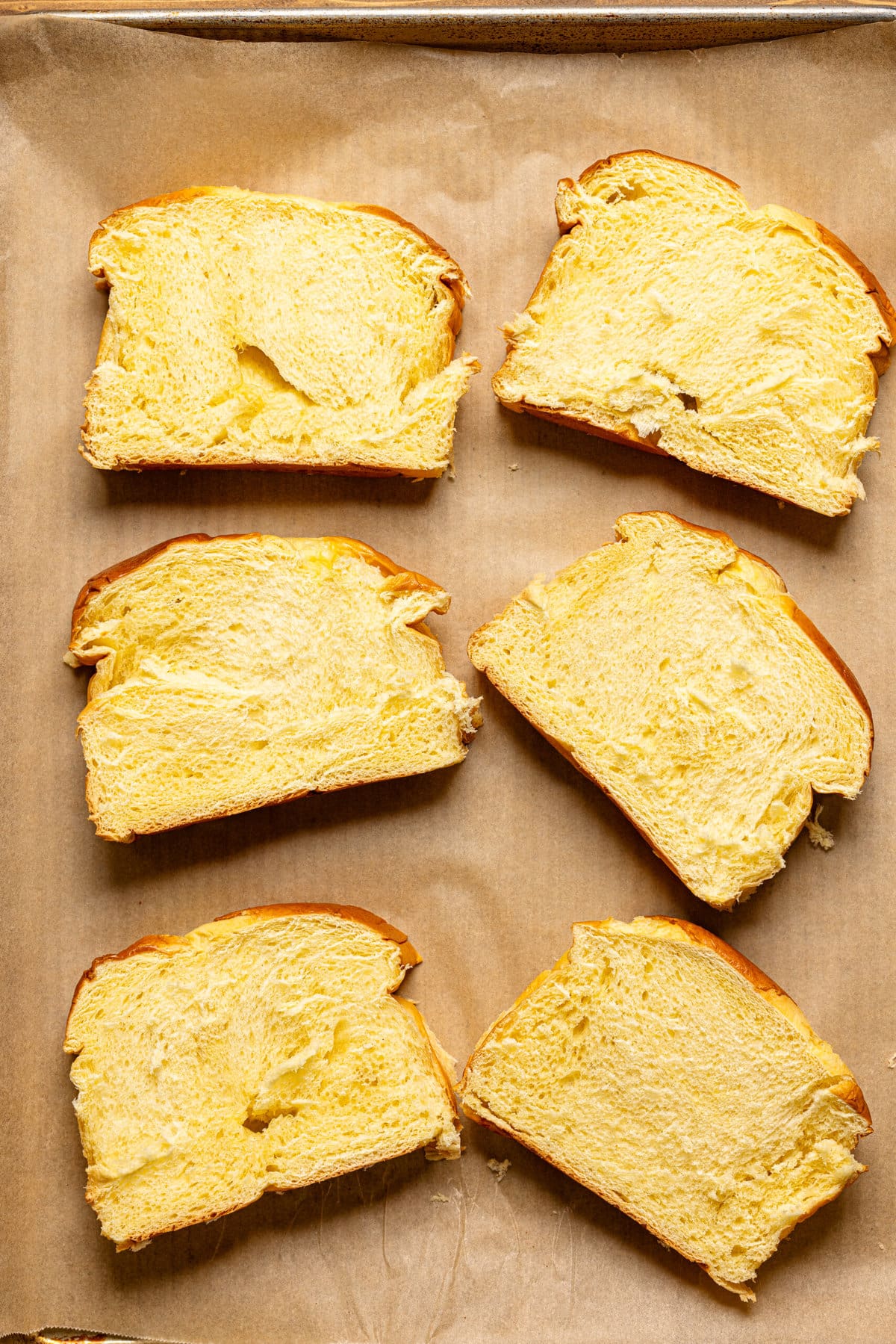 Sliced bread lined side by side on a baking sheet with parchment paper. 