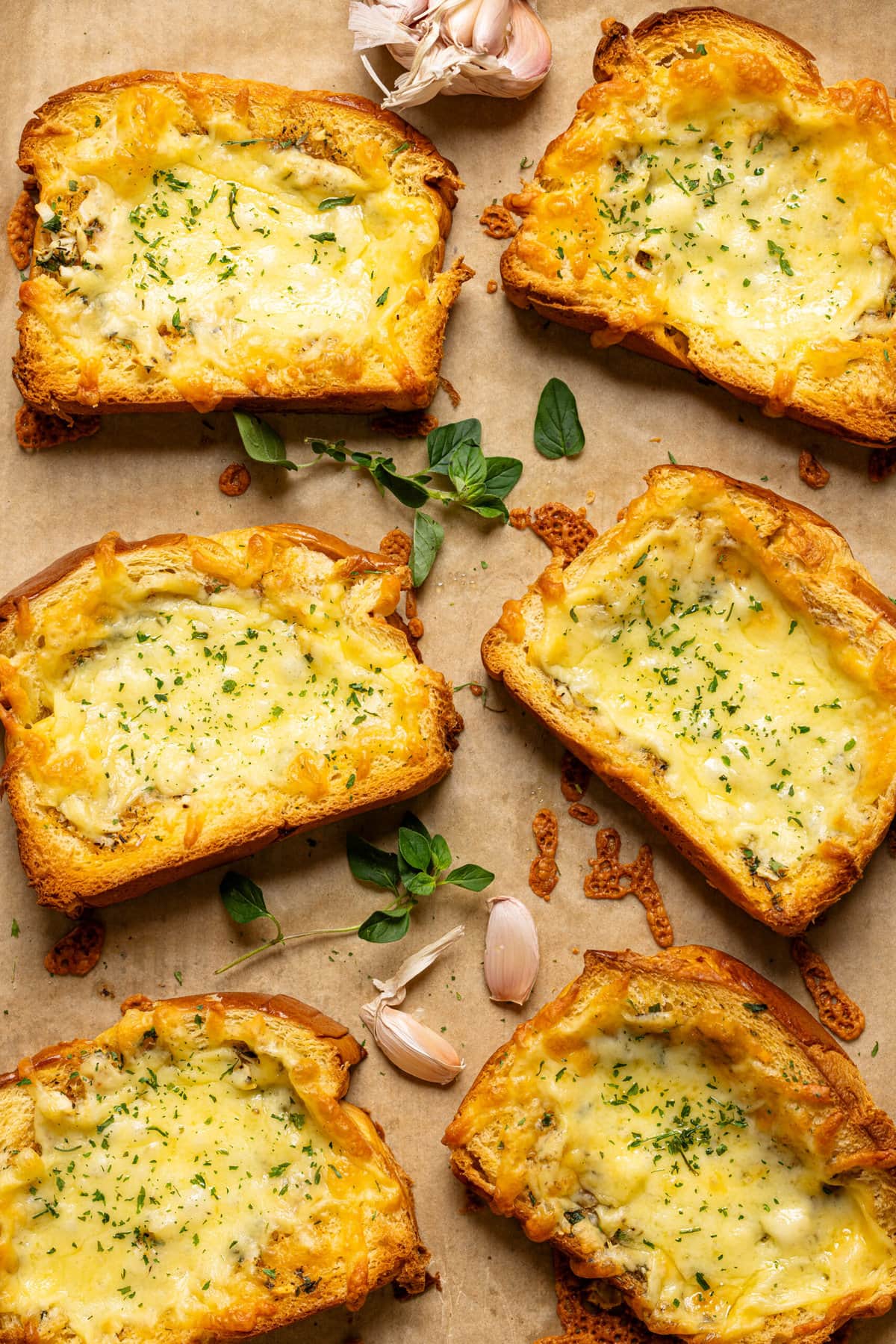 Garlic bread lined side by side on a baking sheet with parchment paper.