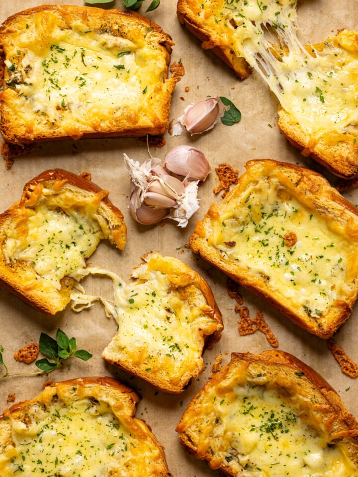 Garlic bread on a baking sheet with parchment paper with garlic cloves + herbs.