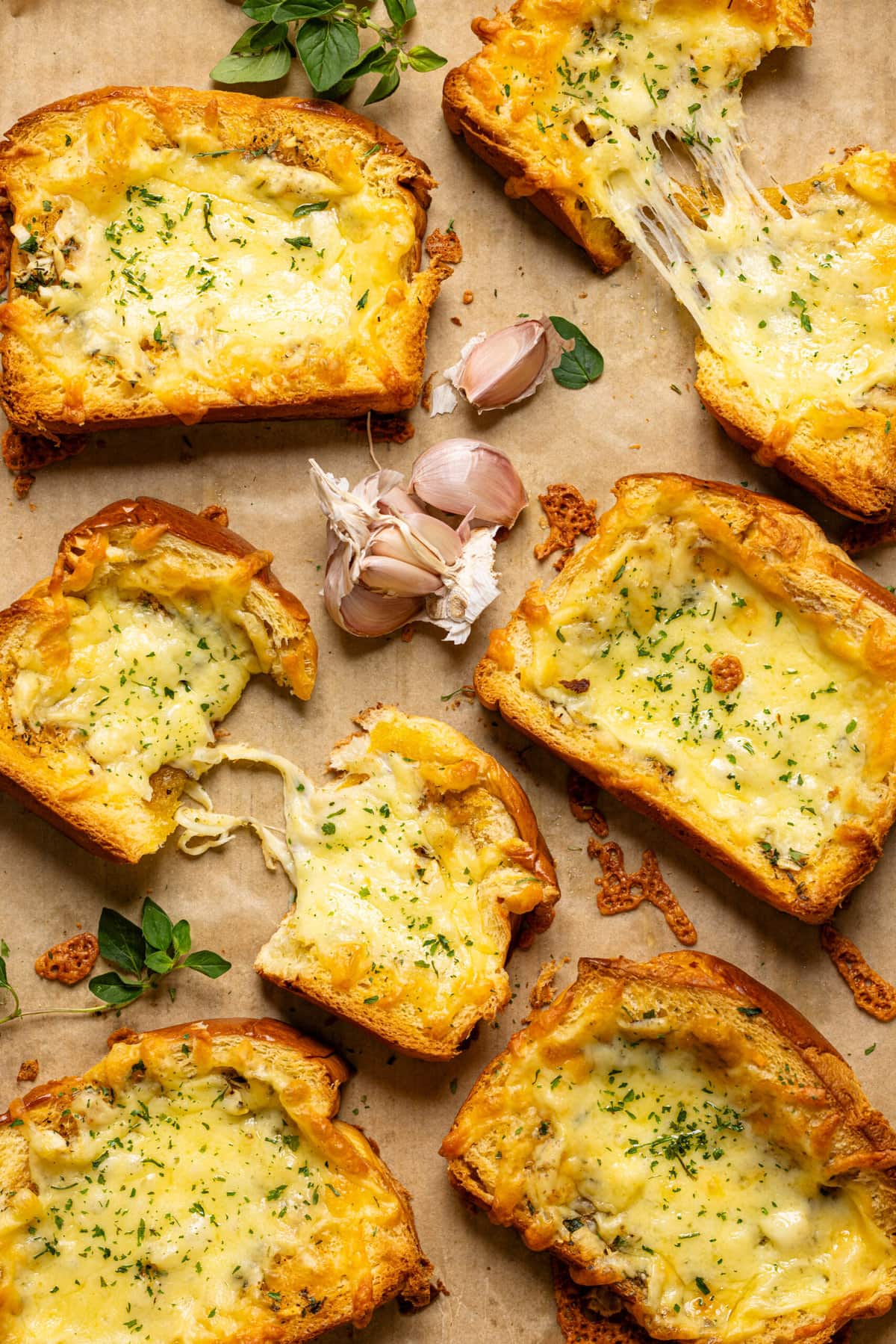 Garlic bread on a baking sheet with parchment paper with garlic cloves + herbs.