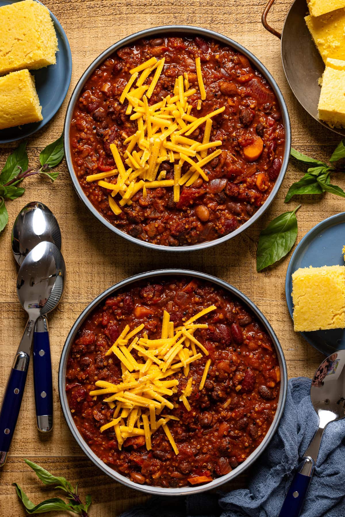 Two bowls with spoons and a side of cornbread. 