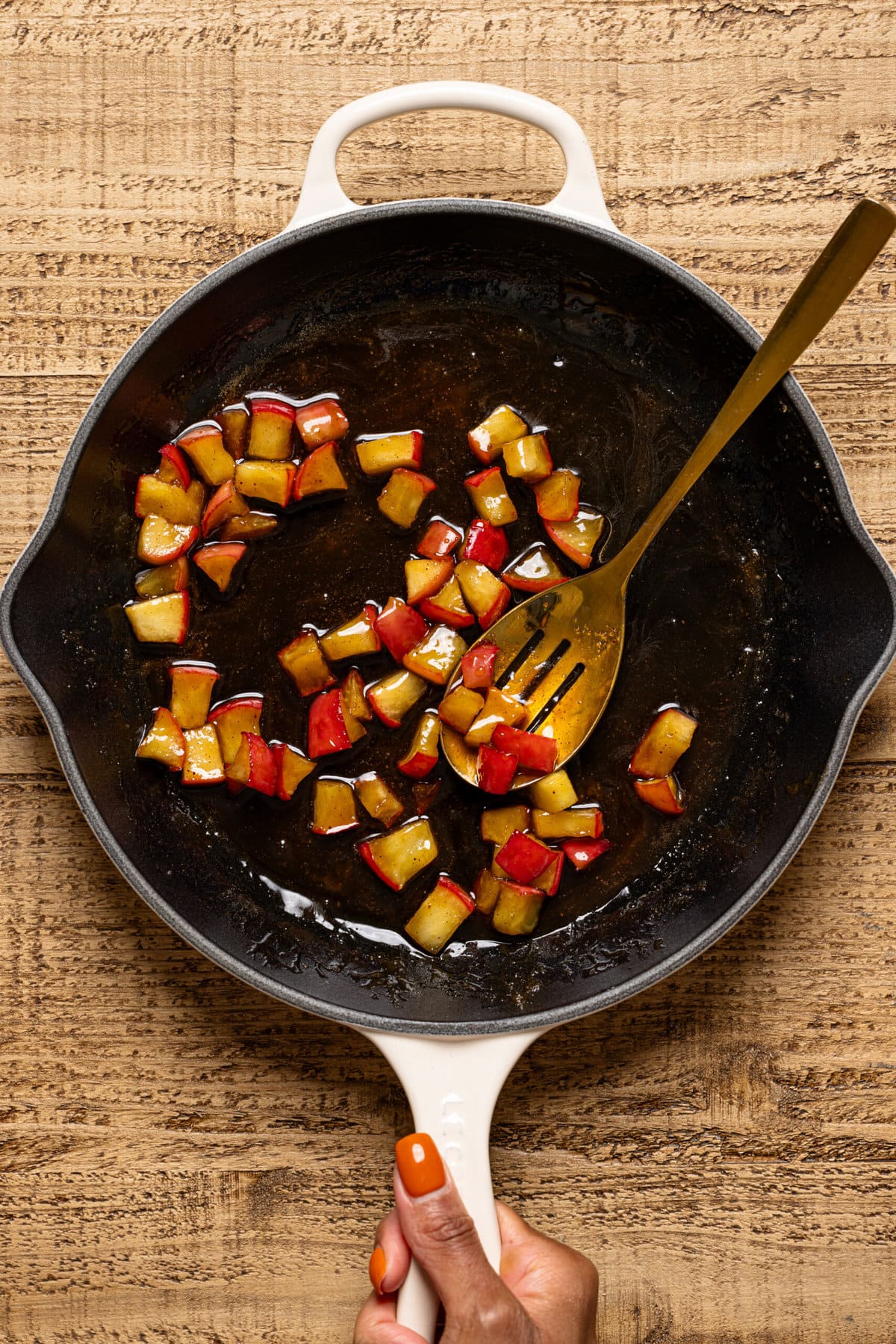Sautéed apples in a white skillet on a brown wood table.
