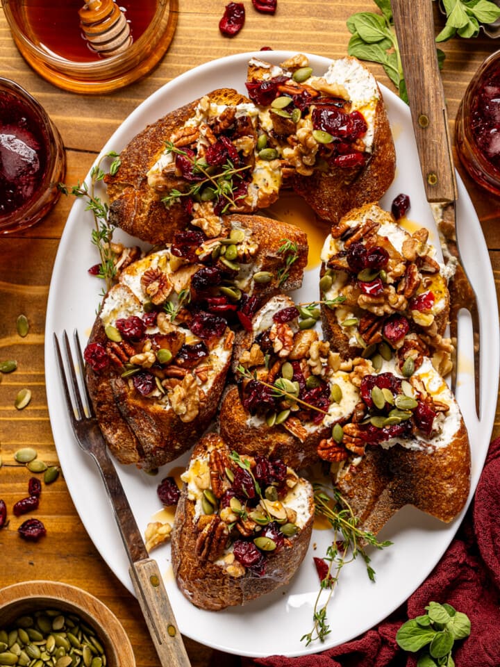 Crostinis on a white platter with forks, a drink, honey, and garnish.