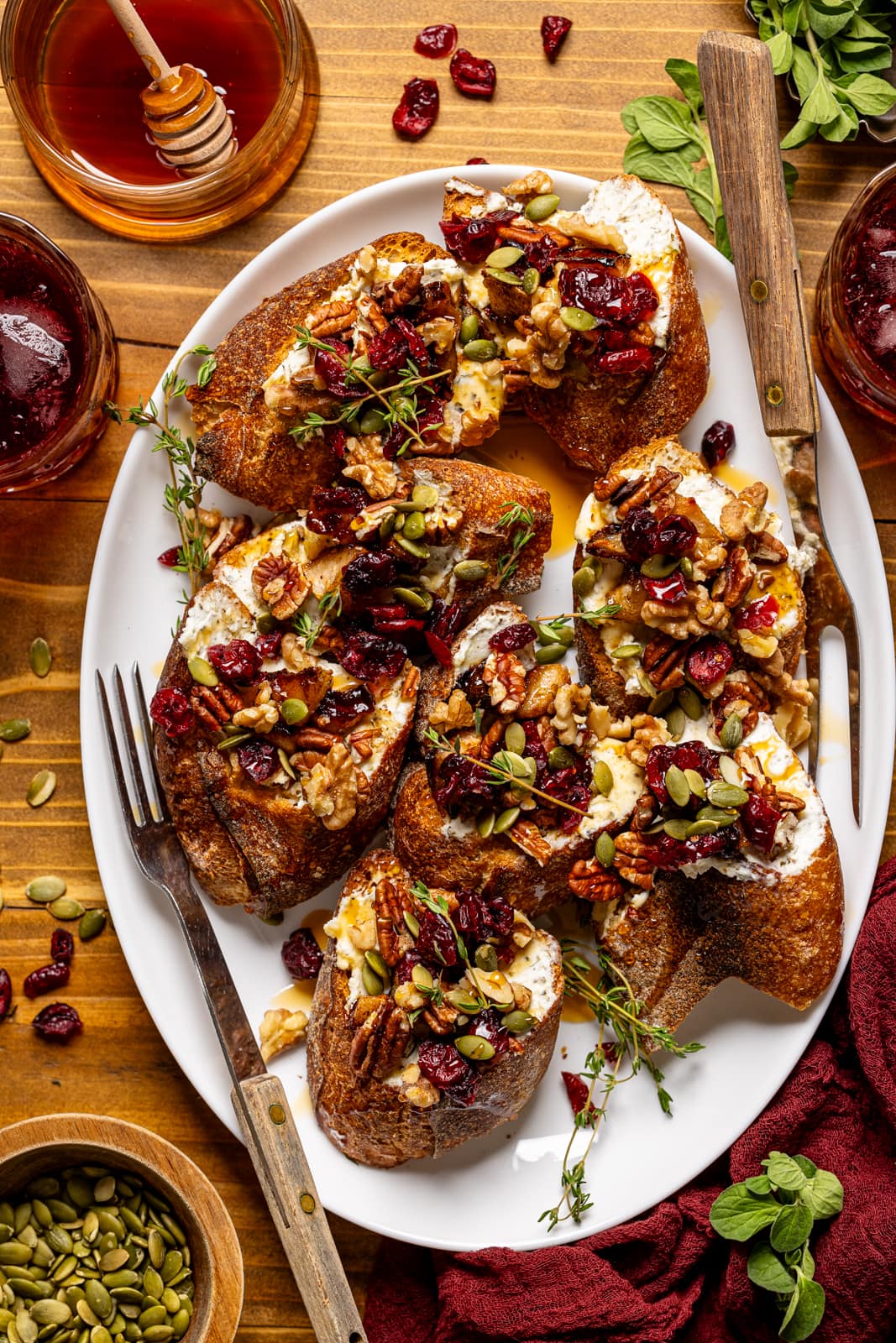 Crostinis on a white platter with forks, a drink, honey, and garnish. Perfect for you thanksgiving menu