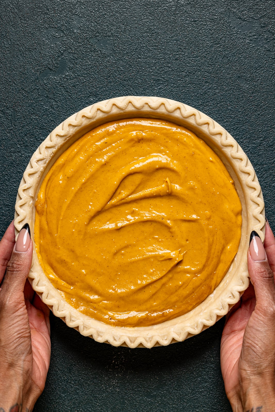 Pie filling in a crust being held on a dark green table. 