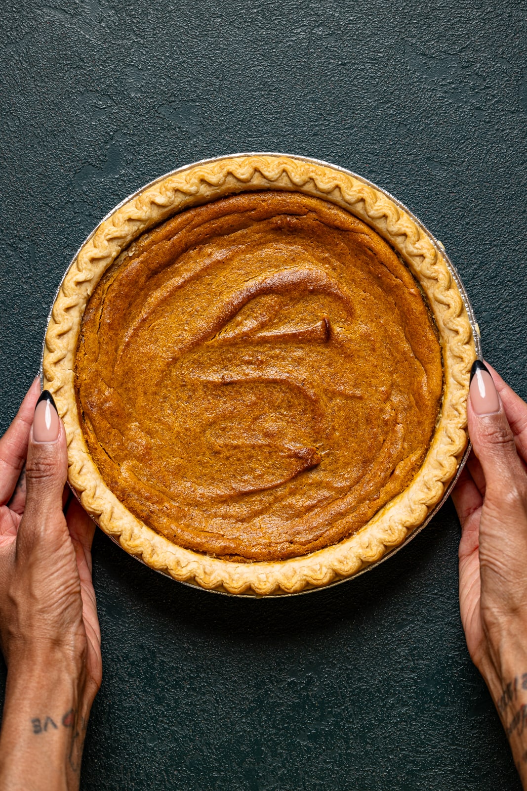 Baked pie being held on a dark green table.