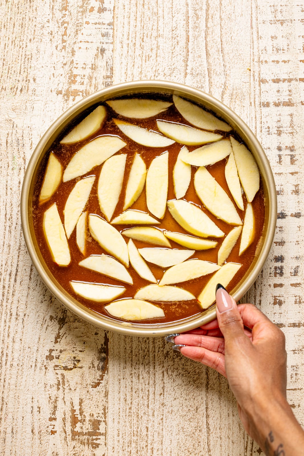 Apple slices with caramel sauce in a round cake pan.