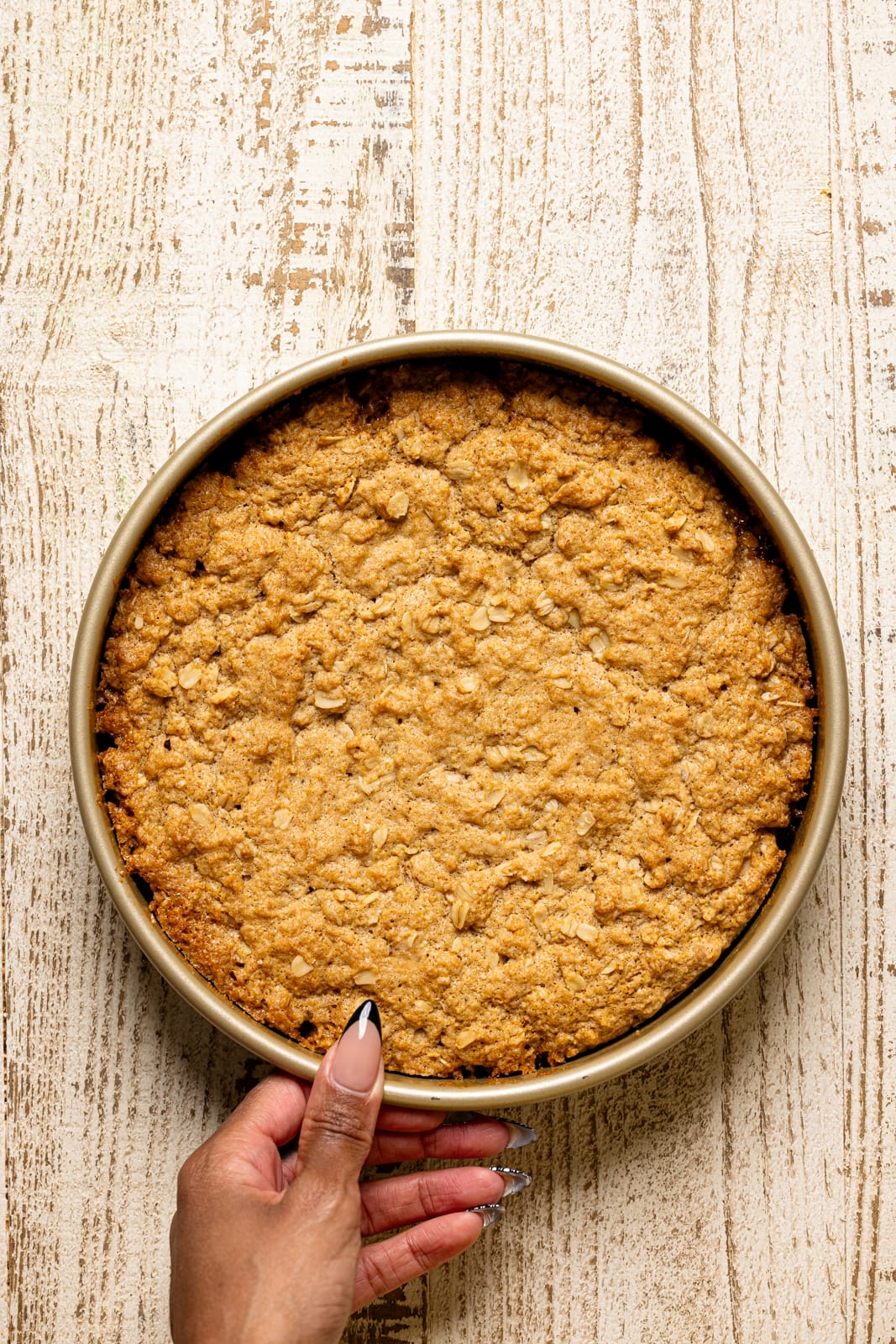 Baked cake in a round cake pan on a white wood table.