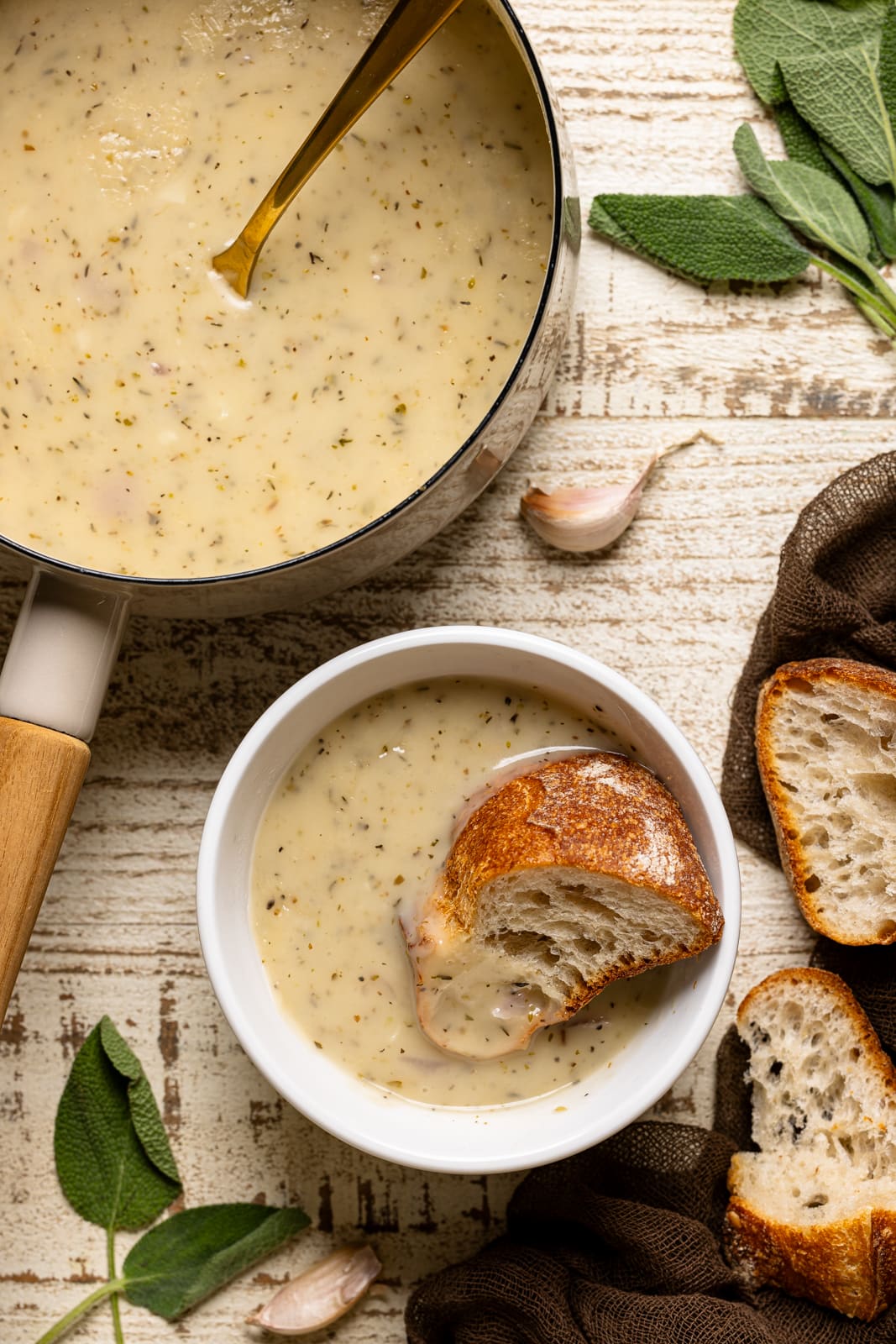 A bowl of gravy with a bread dipped in it with a pot of gravy on the side.