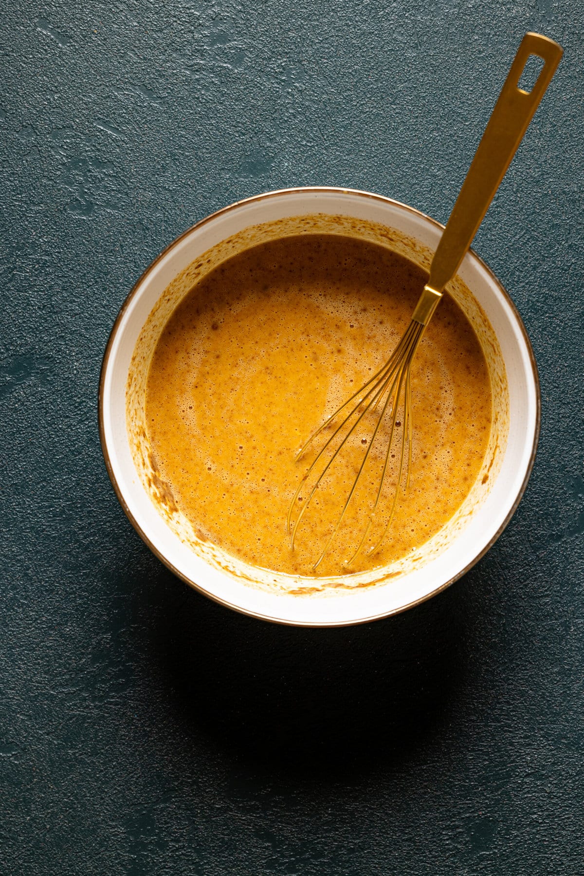 Batter in a white bowl with a gold whisk.