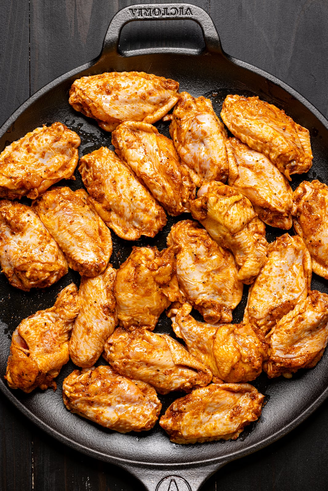 Seasoned chicken wings on a flat black skillet.