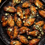 Baked wings on a skillet with a side of bread and garnish.