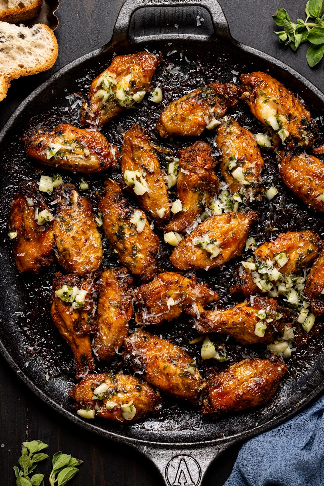 Baked wings on a skillet with a side of bread and garnish. 