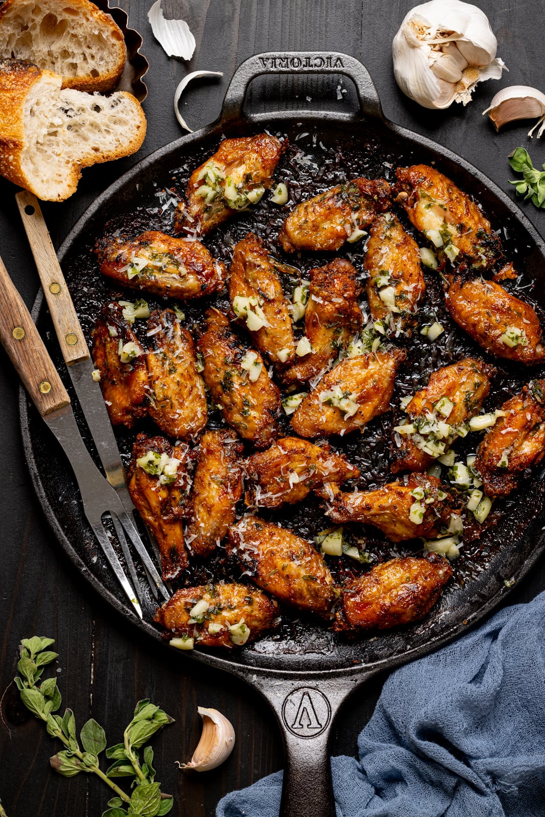 Baked chicken on a black skillet with two forks and garlic. 