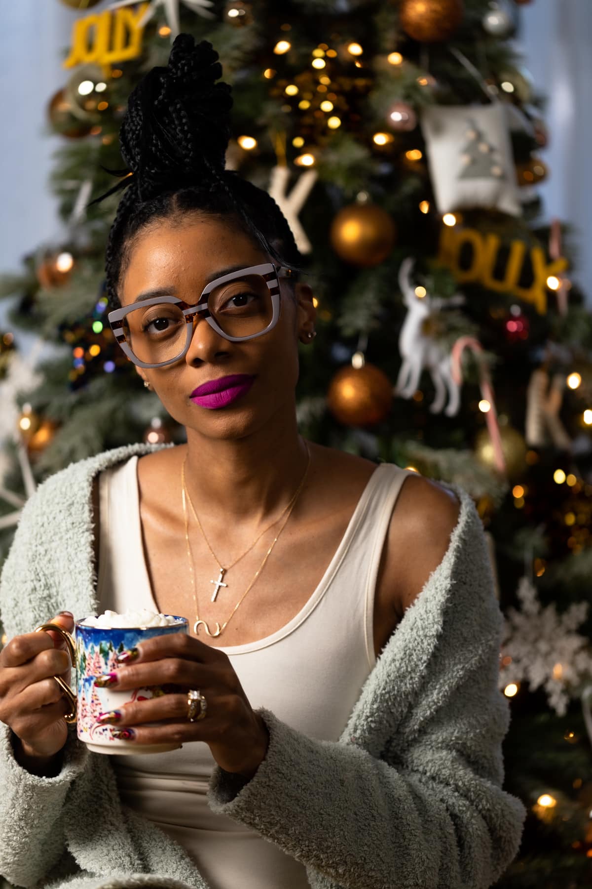 Shanika in front of a Christmas tree holding a mug.