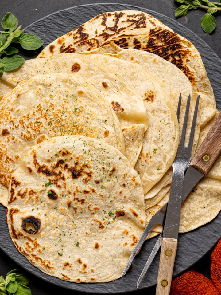 Up close shot of tortillas on a black plate with two forks.