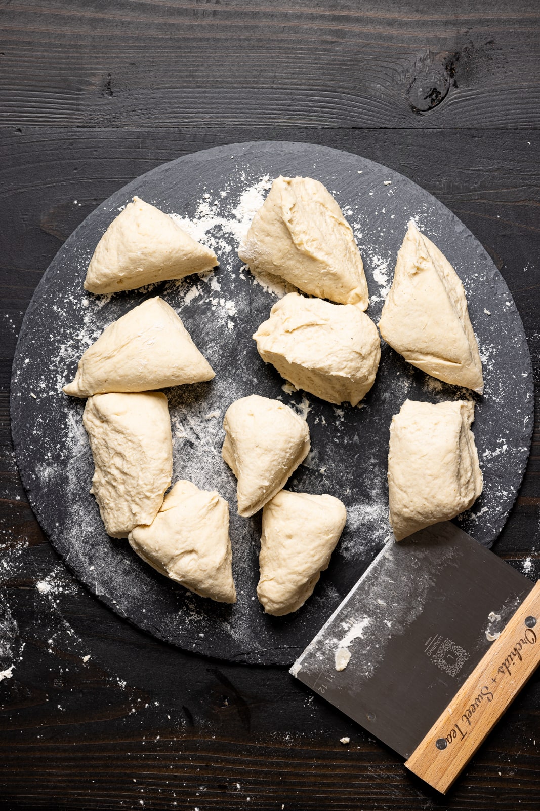 Dough cut into pieces on a black stone platter using a dough scraper. 