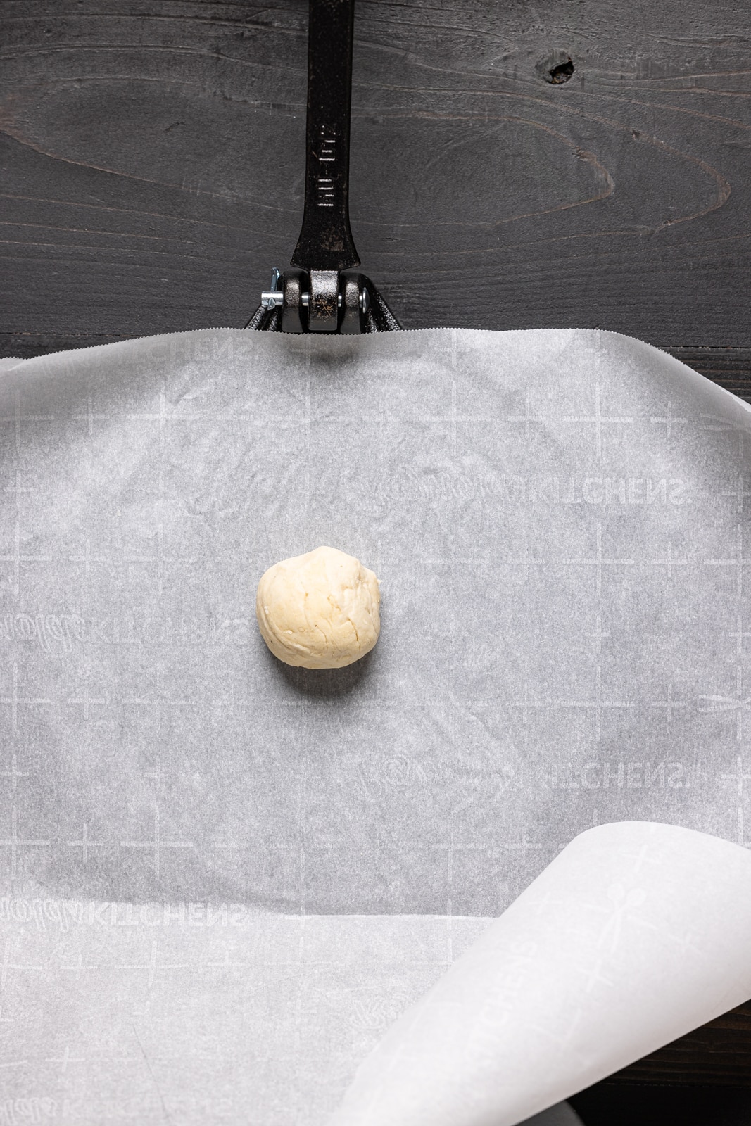 Flour dough ball on a parchment paper on a tortilla press.