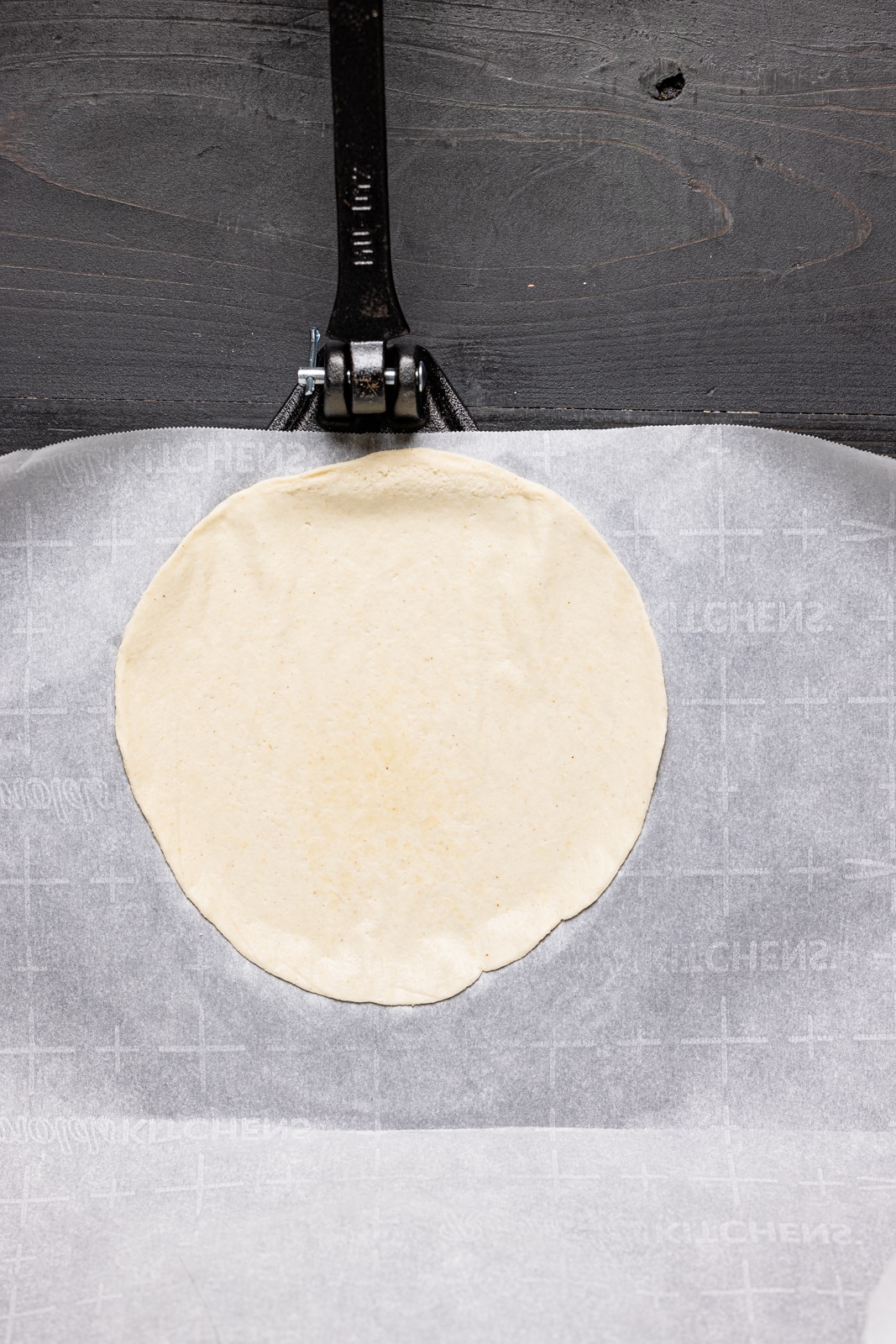 Flattened tortilla dough on parchment paper.