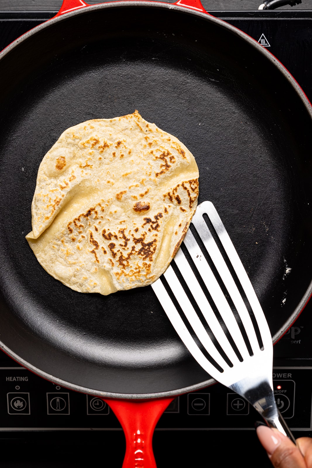 Tortilla being heated in a red skillet being flipped with a spatula. 
