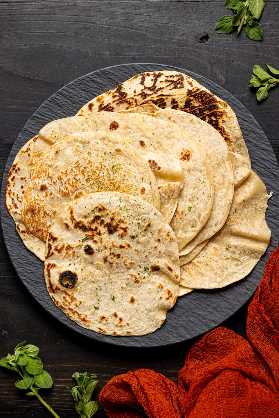 Tortillas on a black plate atop a black wood table.