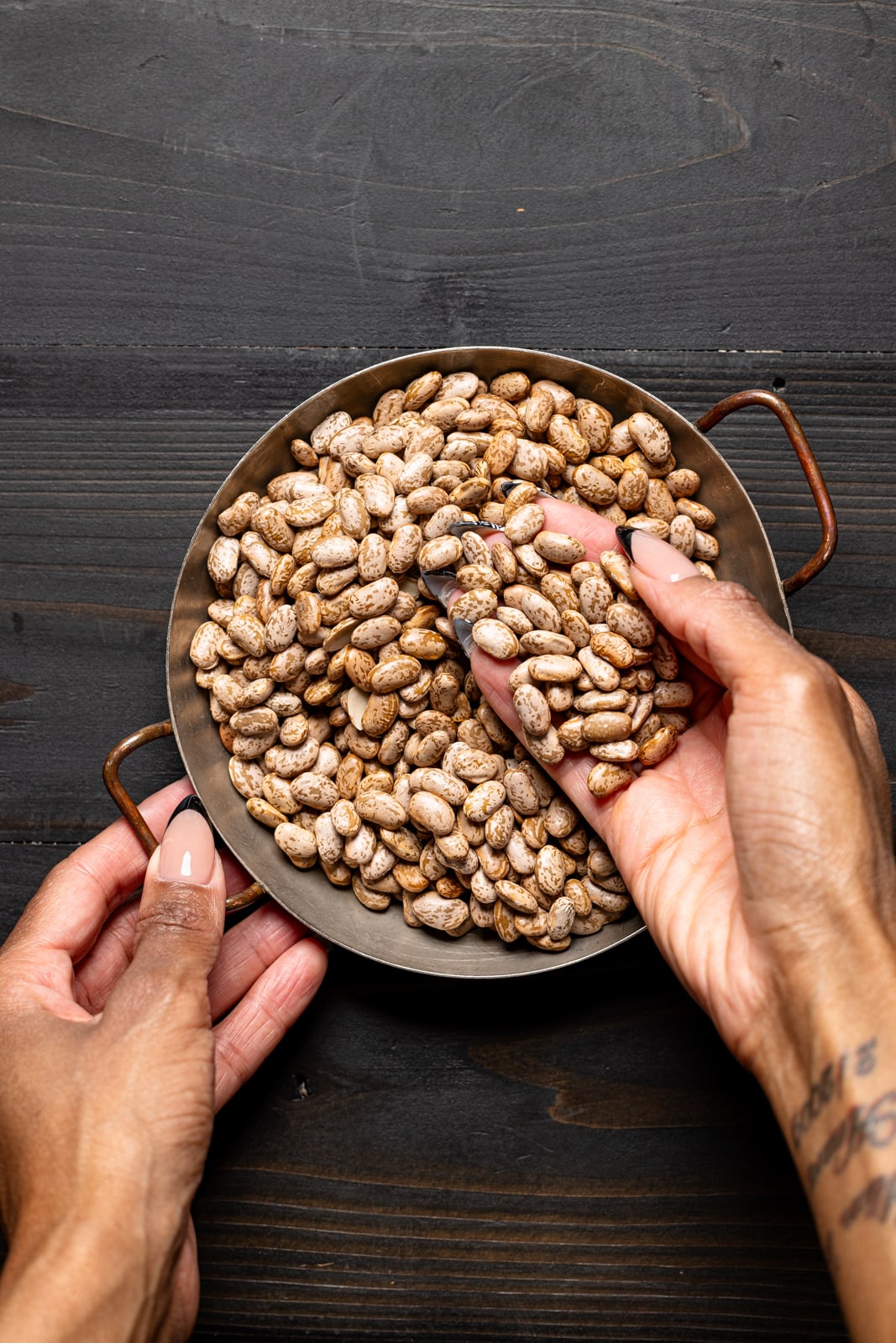 Dried pinto beans in a bowl being held with hands.