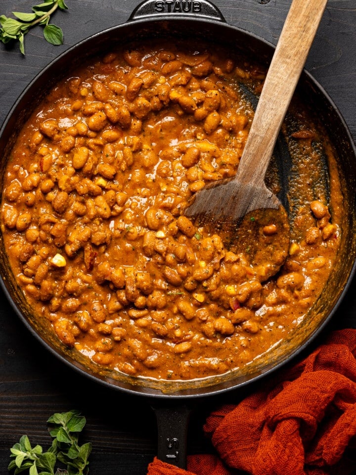 Cooked pinto beans in a black skillet with a wooden spoon.
