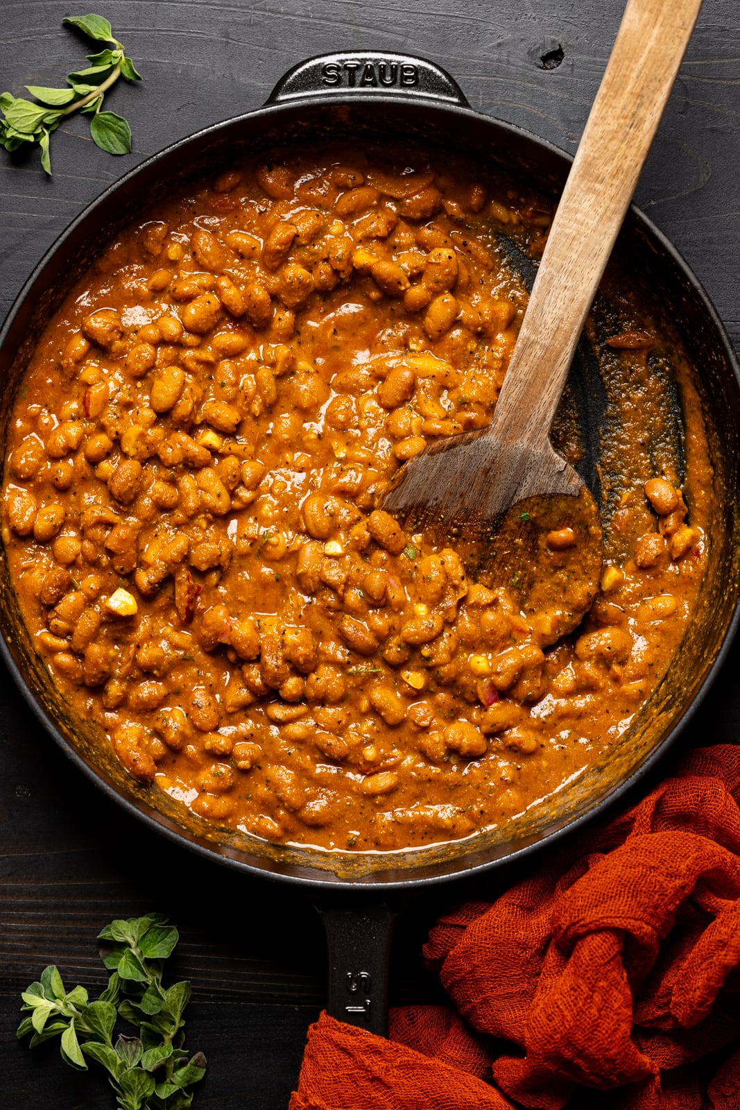 Cooked pinto beans in a black skillet with a wooden spoon.