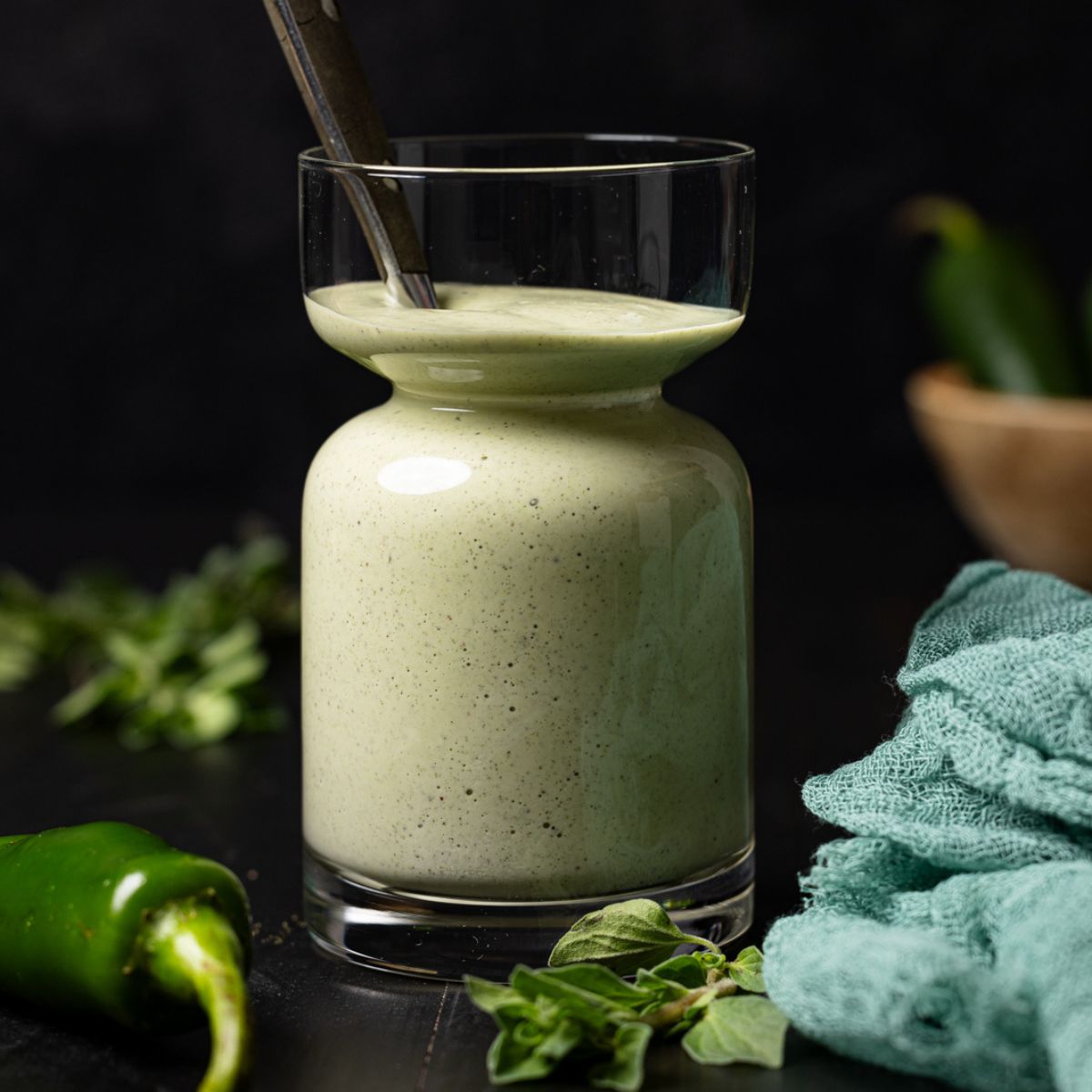 Sauce in a jar with a spoon and jalapenos.