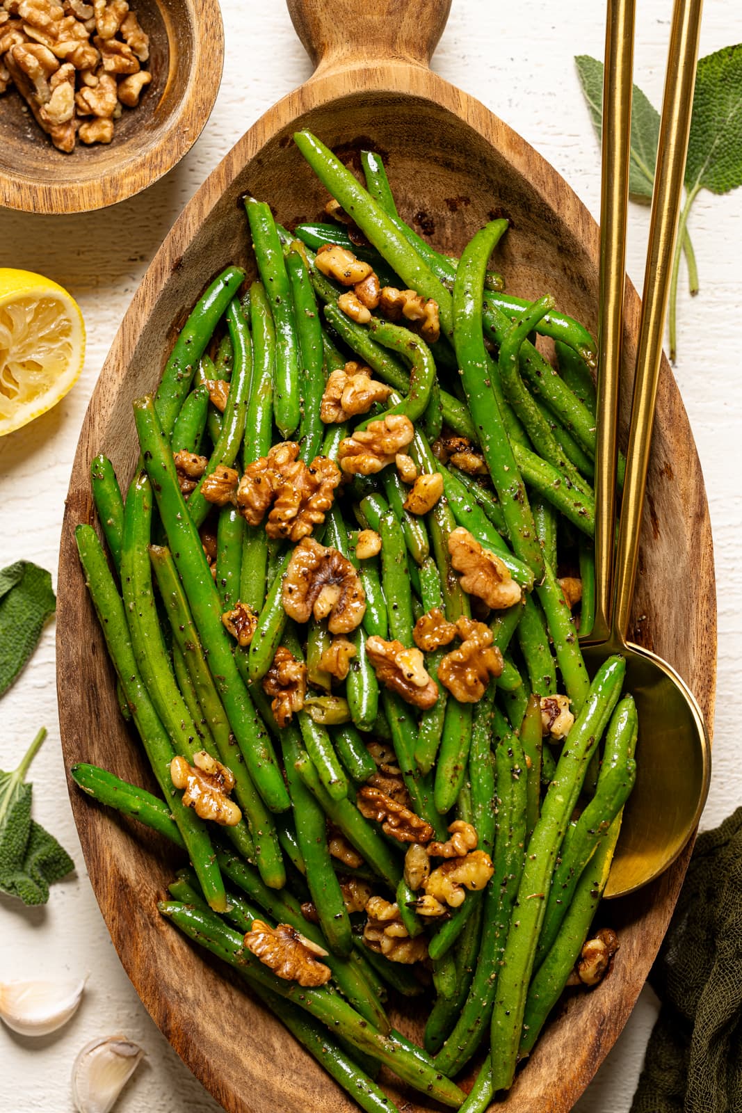 Green beans in a wooden serving platter with two gold spoons.